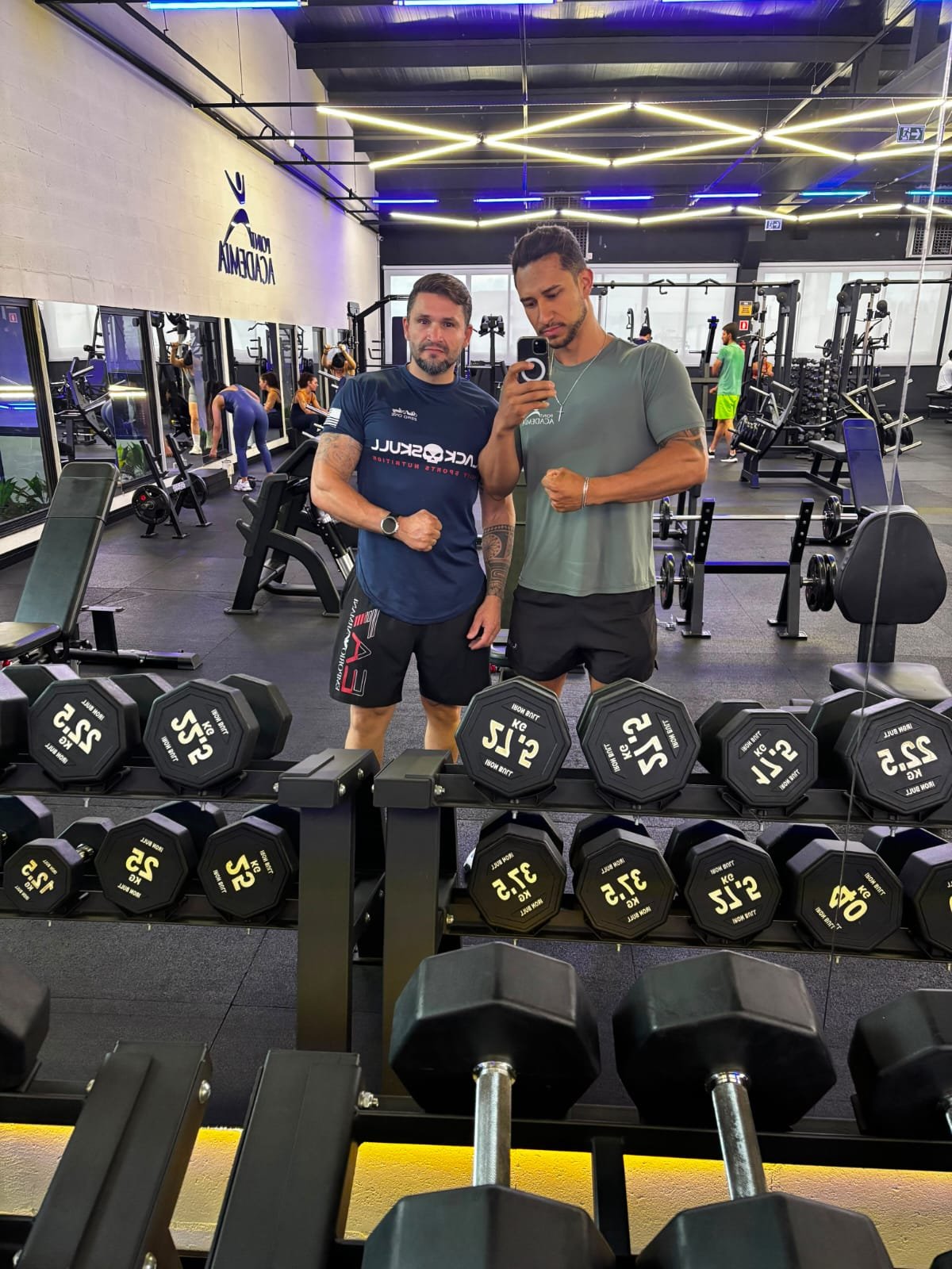 Paulo Henrique ao lado de um aluno em frente ao espelho da academia